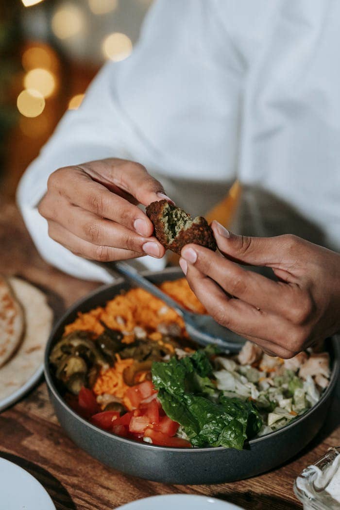 Hands breaking a falafel over a delicious plate of vegetables and salad, creating a healthy meal.