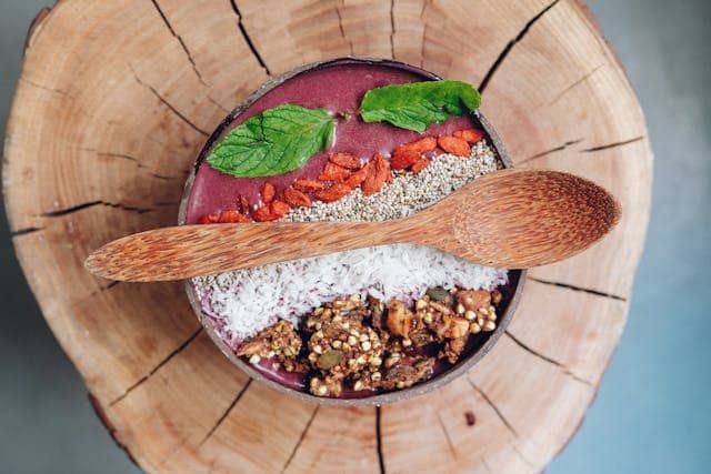 A close-up shot of a vibrant smoothie bowl topped with fresh fruit, granola, and seeds, with a spoon resting beside it.